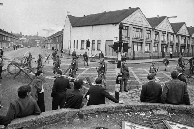 16th August 1969:  Residents watch British troops guarding the entrance of the Falls Road area, behind barbed wire barricades, at Belfast after shootings.  (Photo by Wesley/Keystone/Getty Images)