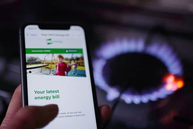 A general view of a household energy bill displayed on a mobile phone held next to a gas hob.