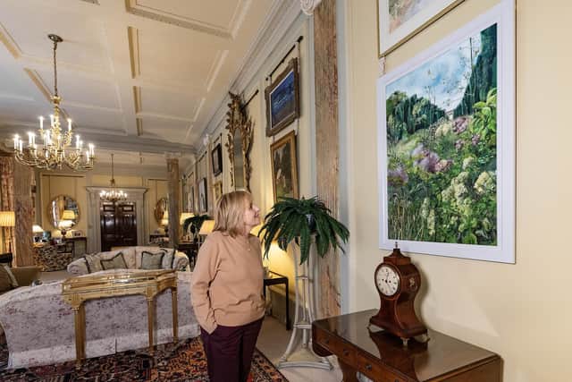 Castle Steward Kim Diver admires a brand new contemporary painting, Late Summer on Yew Tree Walk (2024) by local artist Emma Spence. The painting features in the new re-hang of Irish art in the State Drawing Room at Hillsborough Castle and Gardens, and depicts a scene from Hillsborough's gardens, with the Castle in the distance.