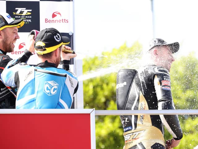 Paul Jordan gets soaked in champagne by Peter Hickman and Lee Johnston after claiming his first Isle of Man TT podium in 2022 in the Supertwin race