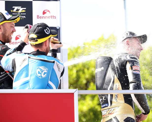 Paul Jordan gets soaked in champagne by Peter Hickman and Lee Johnston after claiming his first Isle of Man TT podium in 2022 in the Supertwin race