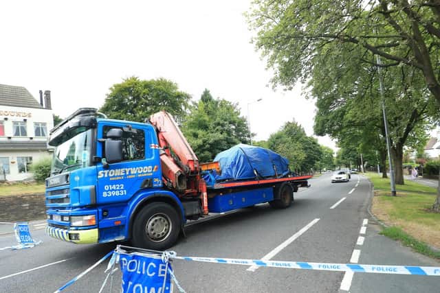 A car covered by a tarpaulin is removed from the scene