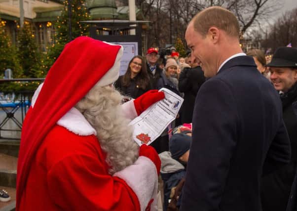 The Duke of Cambridge hands Prince George's Christmas Wish List to a man dressed as Santa Claus as he visits Esplanade Park's Christmas market in Helsinki, on the second day of his tour of Finland