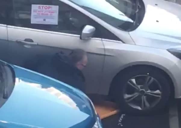 Sinn Fein MLA Gerry Kelly removing a wheel clamp from a car parked in Belfast city centre