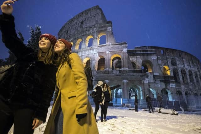 Two women take a selfie in front of the ancient Colosseum during a snowfall, early Monday