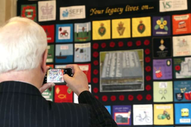 A visitor takes a picture of a memorial quilt, where each patch honours a victim