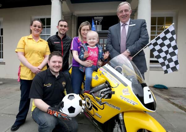 Little Clodagh McNamee and her mother, Ciara, with the Joeys Bar MCC 125 Honda during a visit by Nikki Coates (second from left) and Gary Dunlop (front) who staged a charity football match in aid of the Childrens Cancer Unit Charity. They are pictured here with Play Specialist, Francine McDonald and Wallace McFall from Charles Hurst, who sponsored the event.
