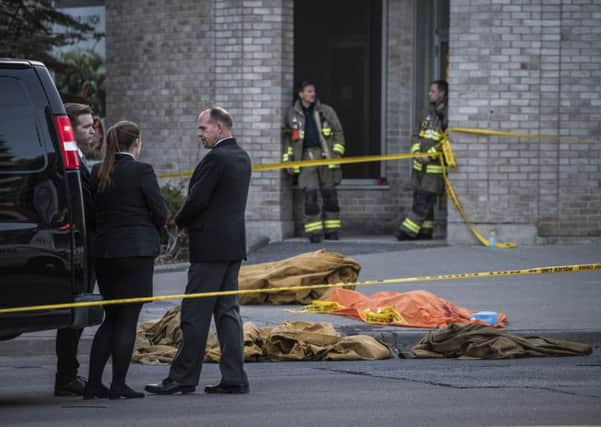 A coroner waits to remove a dead body from the sidewalk after a driver plowed a rented van along a crowded sidewalk, killing multiple people and injuring others on Monday in Toronto.