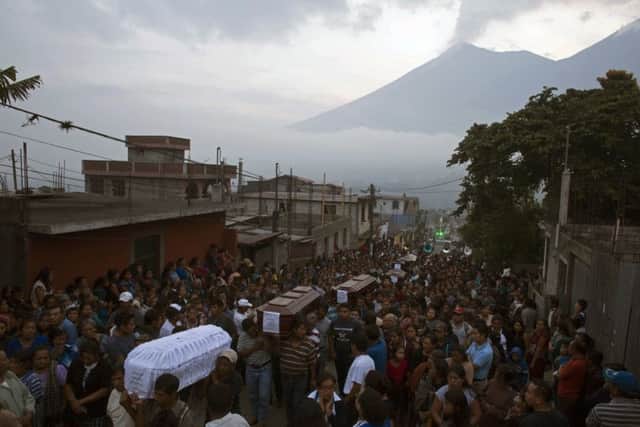 People carry the coffins of seven people who died during the eruption of the Volcan de Fuego, which in Spanish means Volcano of Fire, in the background, to the cemetery in San Juan Alotenango, Guatemala