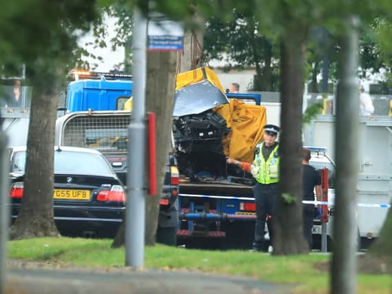A car covered by a tarpaulin is removed from the scene in Bradford following a road traffic collision where four males died in a car which was being followed by an unmarked police vehicle when it crashed.