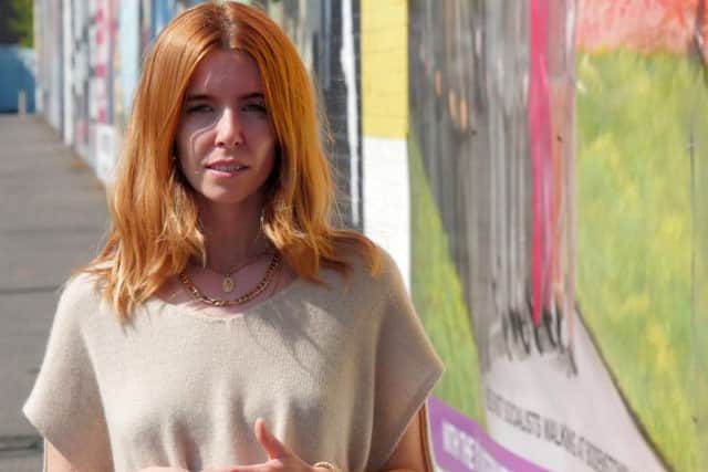 Stacey Dooley pictured standing next to murals at the Lower Falls Road, Belfast. (C) BBC - Photographer: Joseph McAuley