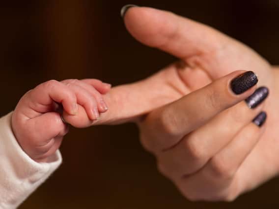 A baby holding its mother's finger.