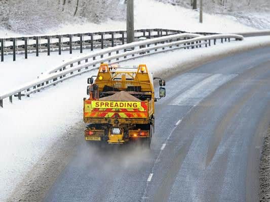 A gritter spreads salt on a snow covered road.