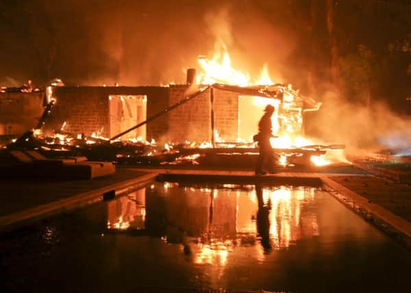 A firefighter walks by the a burning home in Malibu, California as the wildfire continues to burn homes as it runs toward the sea. Winds are blamed for pushing the fire through scenic canyon communities and ridgetop homes. (AP Photo/Ringo H.W. Chiu)