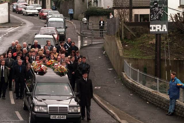 People follow the coffin of Eamon Collins as his cortege makes his way through Newry this afternoon, under the glare of an IRA gunman on a sign