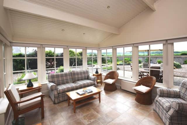 The sun room which features a tiled floor, wood panelled vaulted ceiling, bespoke glass panelled doors with stone archway and access to a paved patio area.