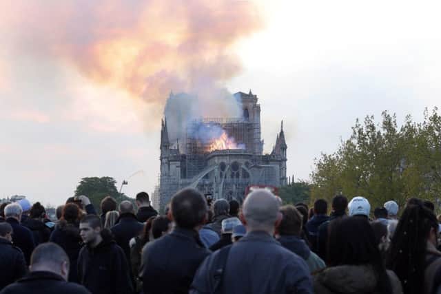 People watch as flames and smoke rise from Notre Dame cathedral as it burns in Paris, Monday, April 15, 2019. Massive plumes of yellow brown smoke is filling the air above Notre Dame Cathedral and ash is falling on tourists and others around the island that marks the center of Paris. (AP Photo/Thibault Camus)