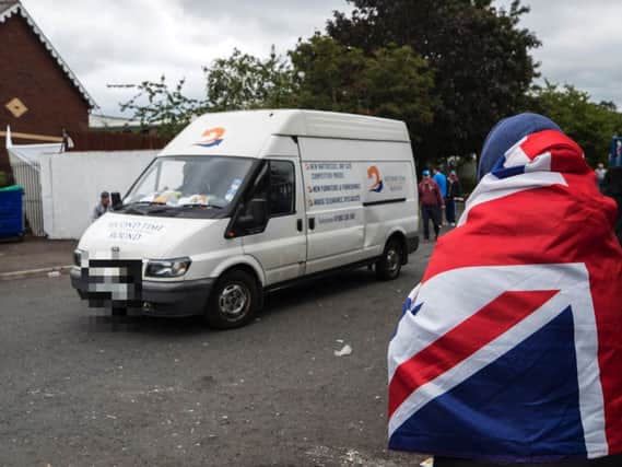 A woman wrapped in a Union flag watches a van carrying tyres that were removed from the 11th night bonfire that was erected at Avoniel Leisure Centre.(Photo: Liam McBurney/P.A. Wire)