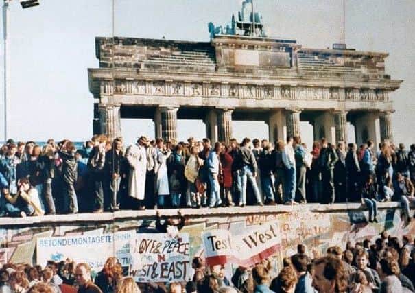 West and East Germans standing on the Berlin Wall at the Brandenburg Gate in 1989