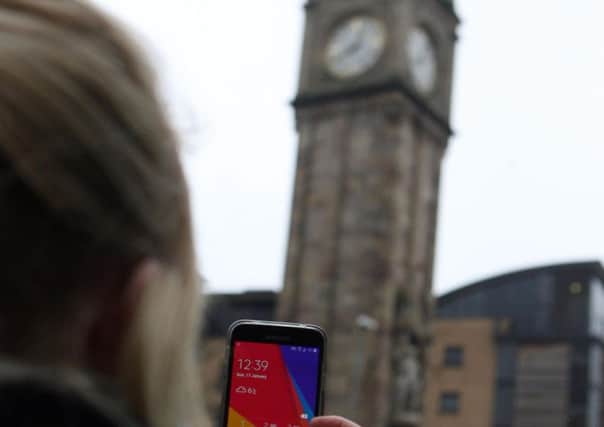 A passerby checks the time on her phone against the newly fixed Albert Clock