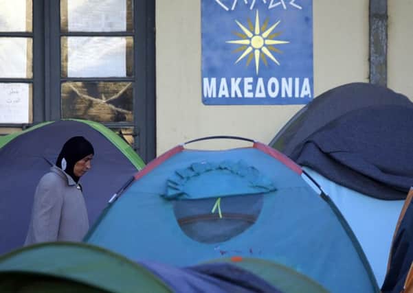 A woman walks through tents and a sign that reads: "Greece-Macedonia" at a railway station turned into a migrants and refugees makeshift camp at the northern Greek border point of Idomeni, Greece