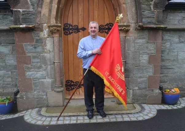The Rector of St Augustines Church, Rev Malcolm Ferry, holds the flag of First Londonderry Scout Troop, which was based at the wee church on the walls until 1972