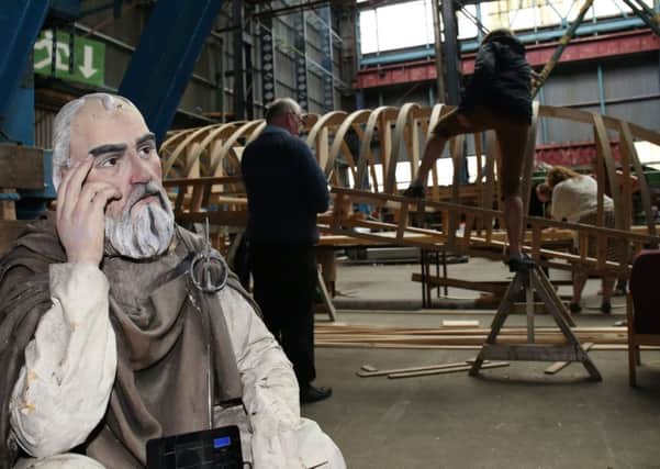 A model of St Columbanus is seen in  the foreground as volunteers take part in the construction of one of the largest currachs ever built, in the Titanic Quarter in Belfast