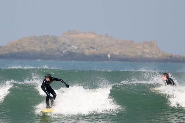 Surfers in action on Portrushs East Strand, with Skerries island in the background