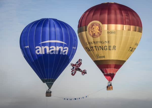 A Pitts Special S2S stunt plane performs the worlds first ever 'knife edge' between two hot air balloons, cutting a ribbon as it passes between them just above the ground at Gloucester airport. Picture: Ben Birchall/PA Wire