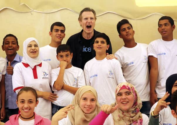Liam Neeson poses for a group photo with Syrian and Jordanian students at a community centre in a working-class neighborhood of Amman, Jordan