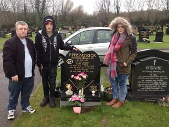Kevin Fitzpatrick with his son James and daughter Ann Marie, standing at the grave of Dana and Kevin Daniel. They were killed by a 'death rider' in Belfast in 2000.