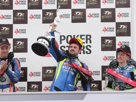 Michael Dunlop raises the Senior TT trophy on the rostrum with runner-up Peter Hickman (left) and Dean Harrison.