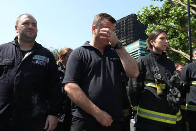 Members of the police and London Fire Brigade observe a minute's silence near to Grenfell Tower (background) in west London after a fire engulfed the 24-storey building on Wednesday morning