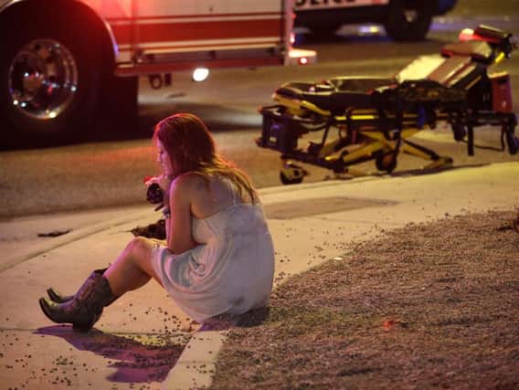 A woman sits on a curb at the scene of a shooting outside of a music festival along the Las Vegas Strip, Monday, Oct. 2, 2017, in Las Vegas. Multiple victims were being transported to hospitals after a shooting late Sunday at a music festival on the Las Vegas Strip. (AP Photo/John Locher)